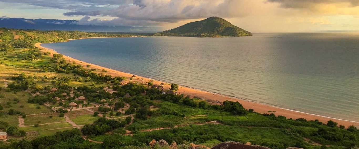 Das Biocamp am Nyasasee Panoramablick auf einen Küstenabschnitt mit Berg im Hintergrund und bewaldeten Ufern.